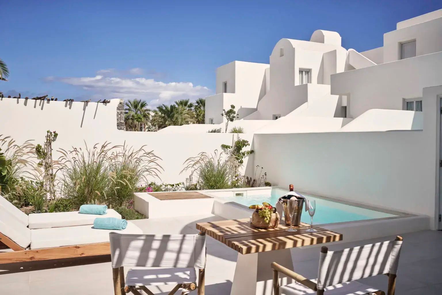 Sonnige Terrasse mit kleinem Pool, Liegestühlen und Blick auf weiße Gebäude.