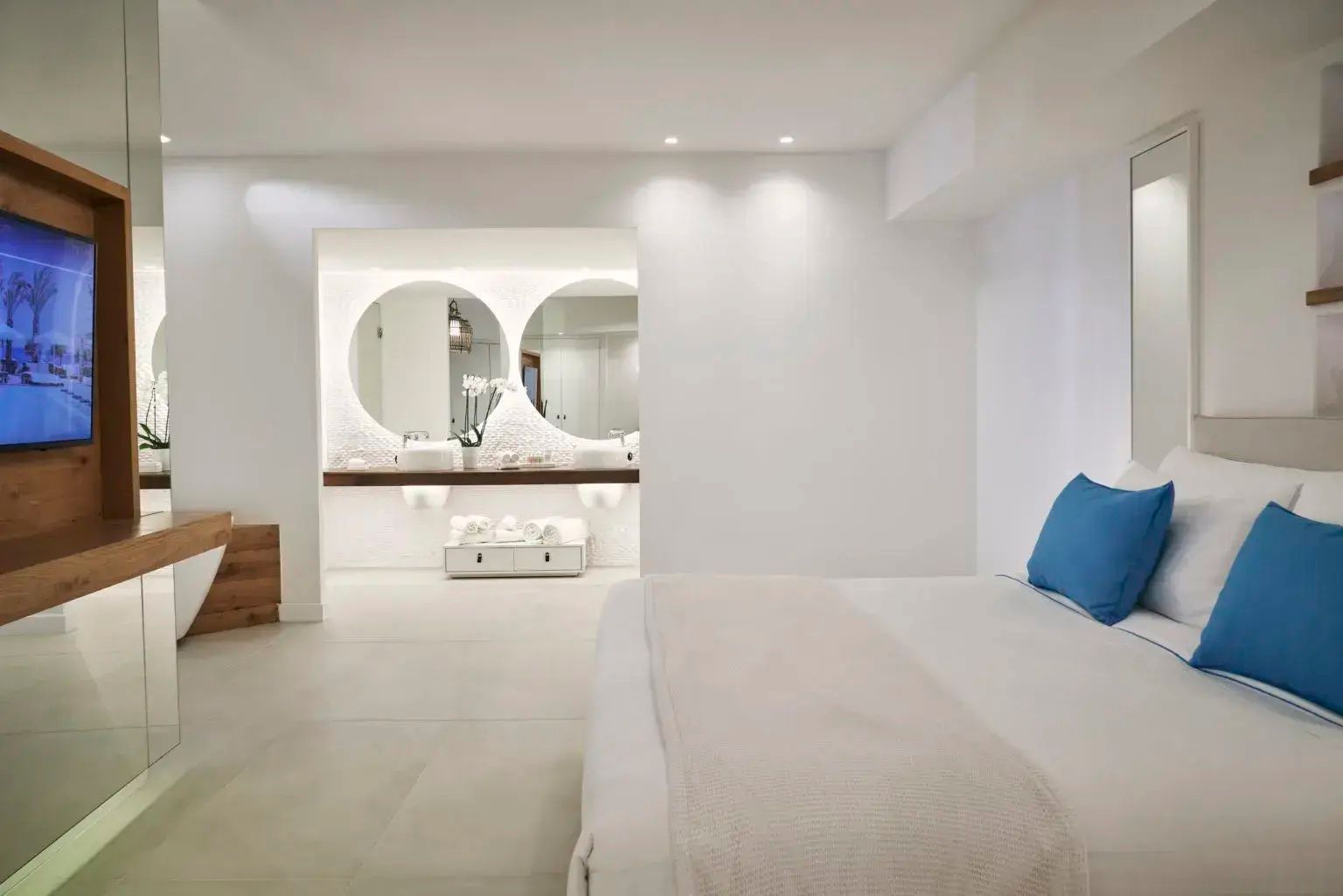 Hell eingerichtetes Hotelzimmer mit Blick auf zwei beleuchtete runde Spiegelelemente über dem Waschtisch.