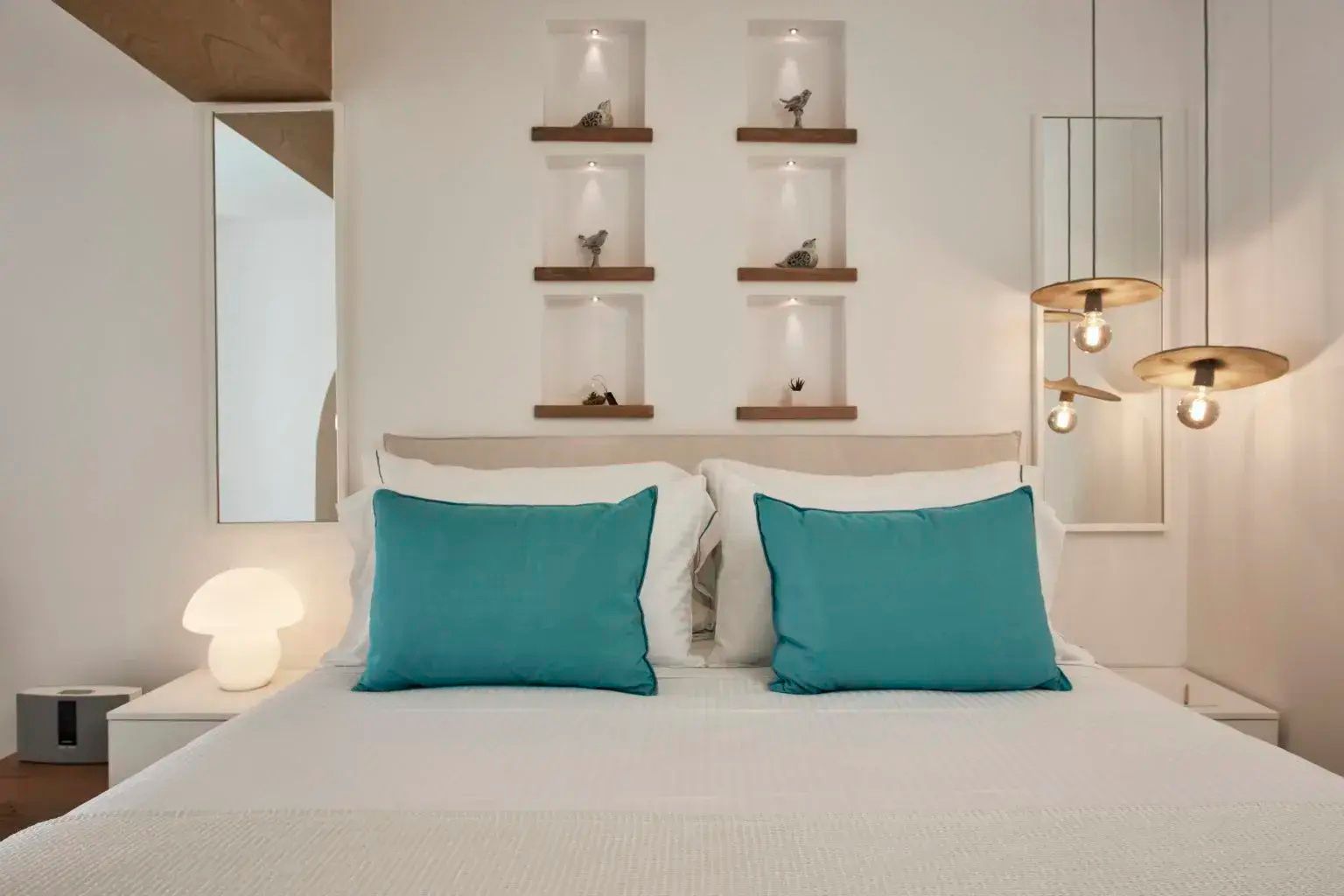 Doppelbett mit türkisfarbenen Kissen und beleuchteten Wandnischen darüber.