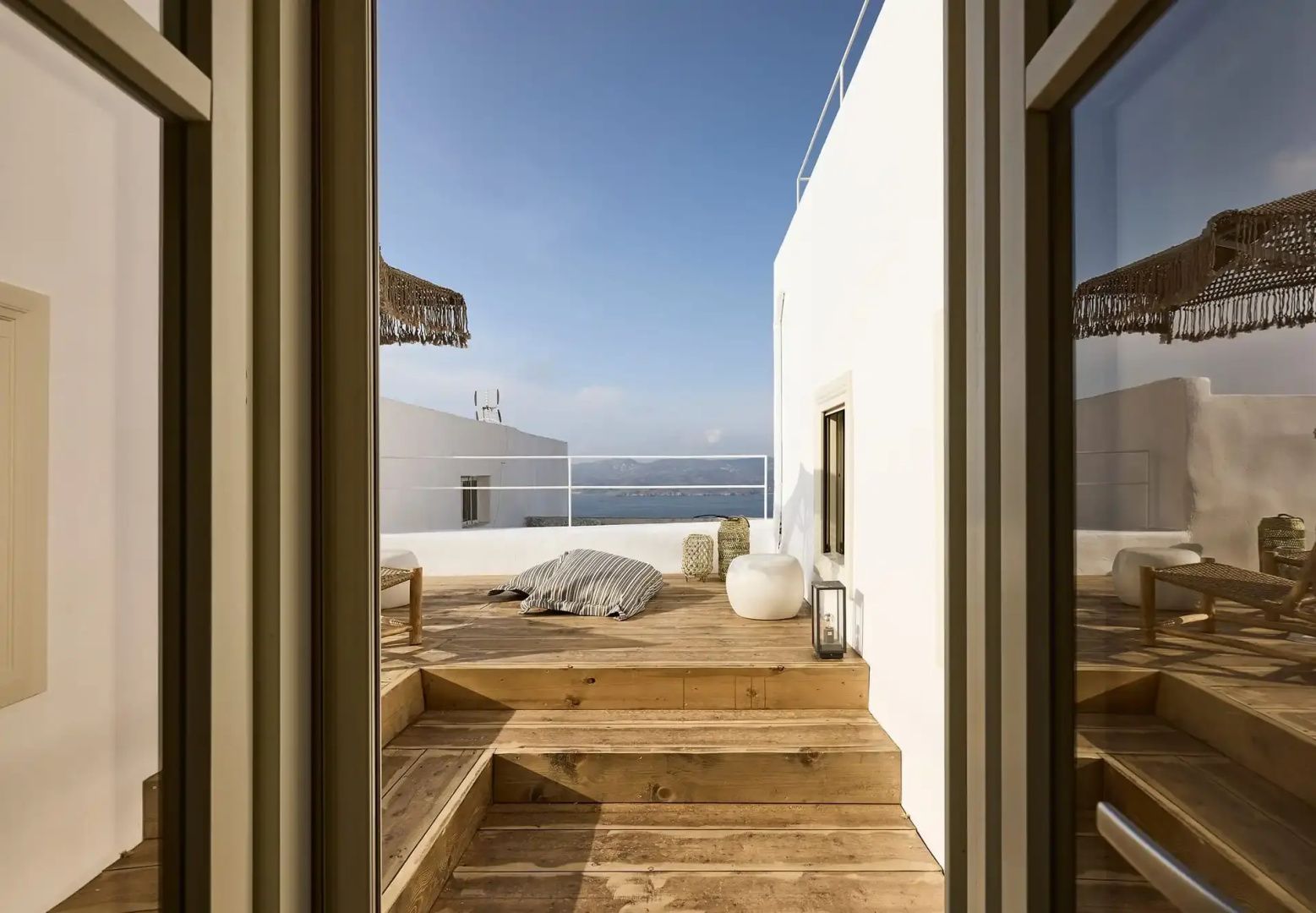 Blick auf eine hölzerne Dachterrasse mit Sitzkissen und Meer im Hintergrund.