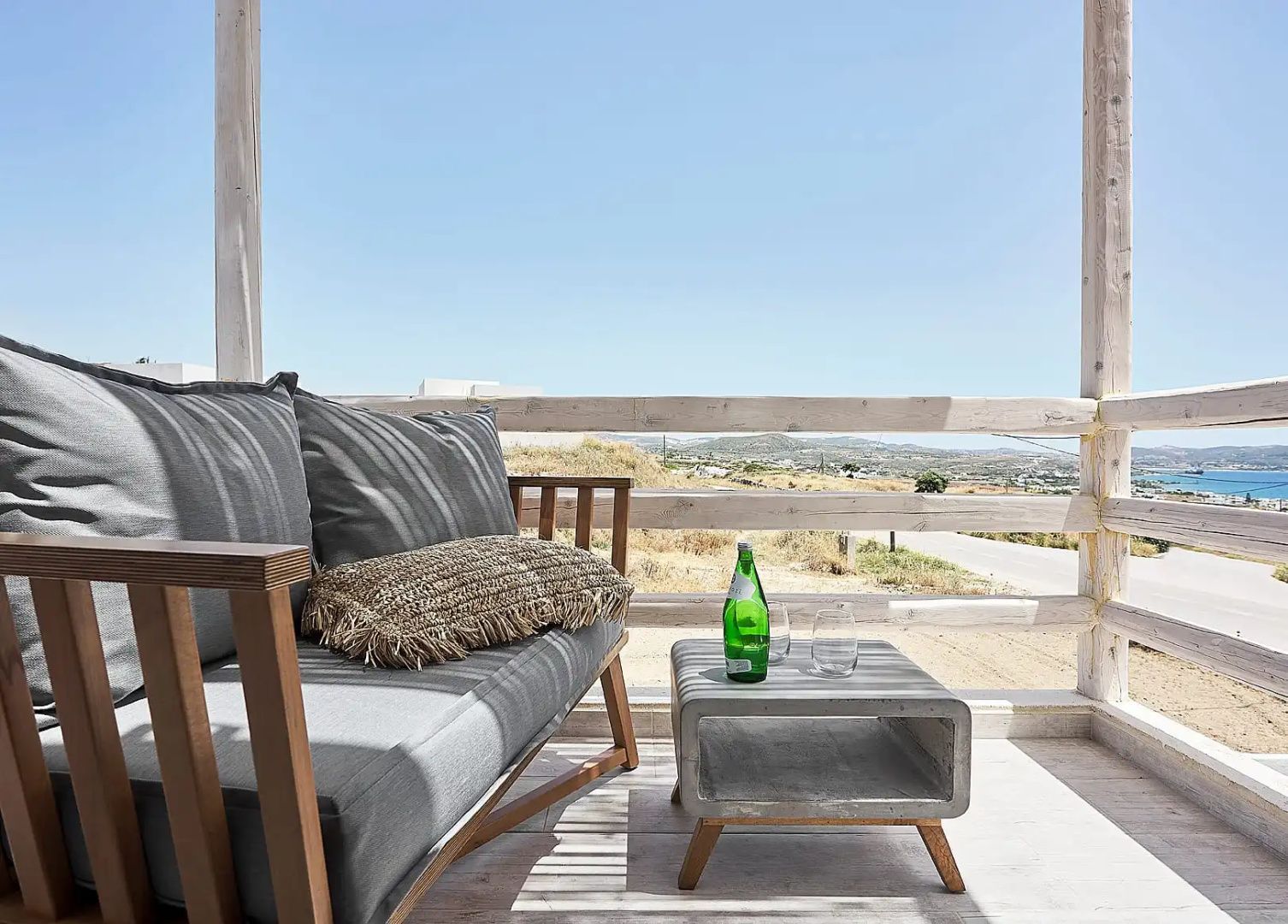 Überdachte Terrasse mit Holzbank, grauem Polster und Beistelltisch mit Blick auf die Landschaft.