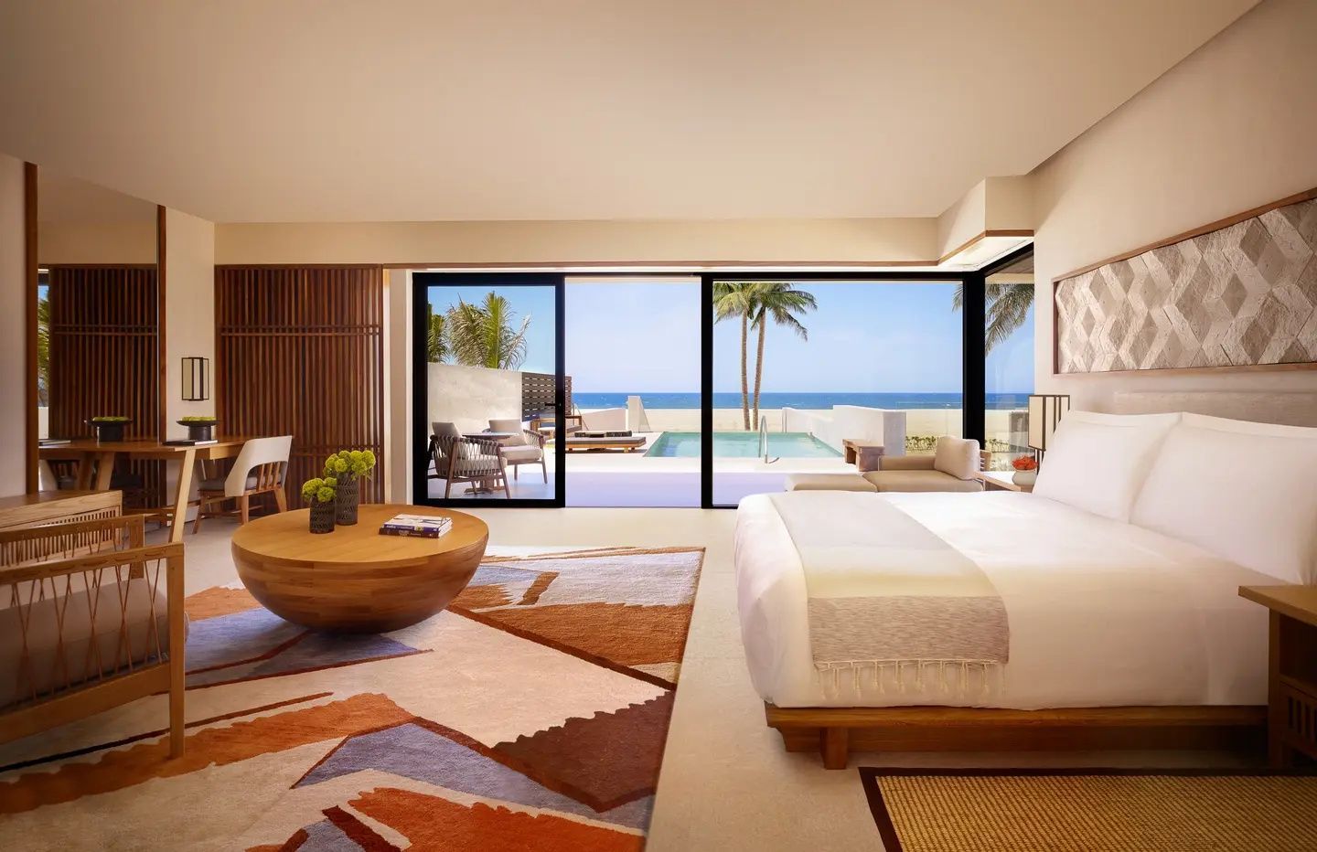 Hell eingerichtetes Schlafzimmer mit Doppelbett, rundem Holztisch und Blick auf Terrasse und Meer.