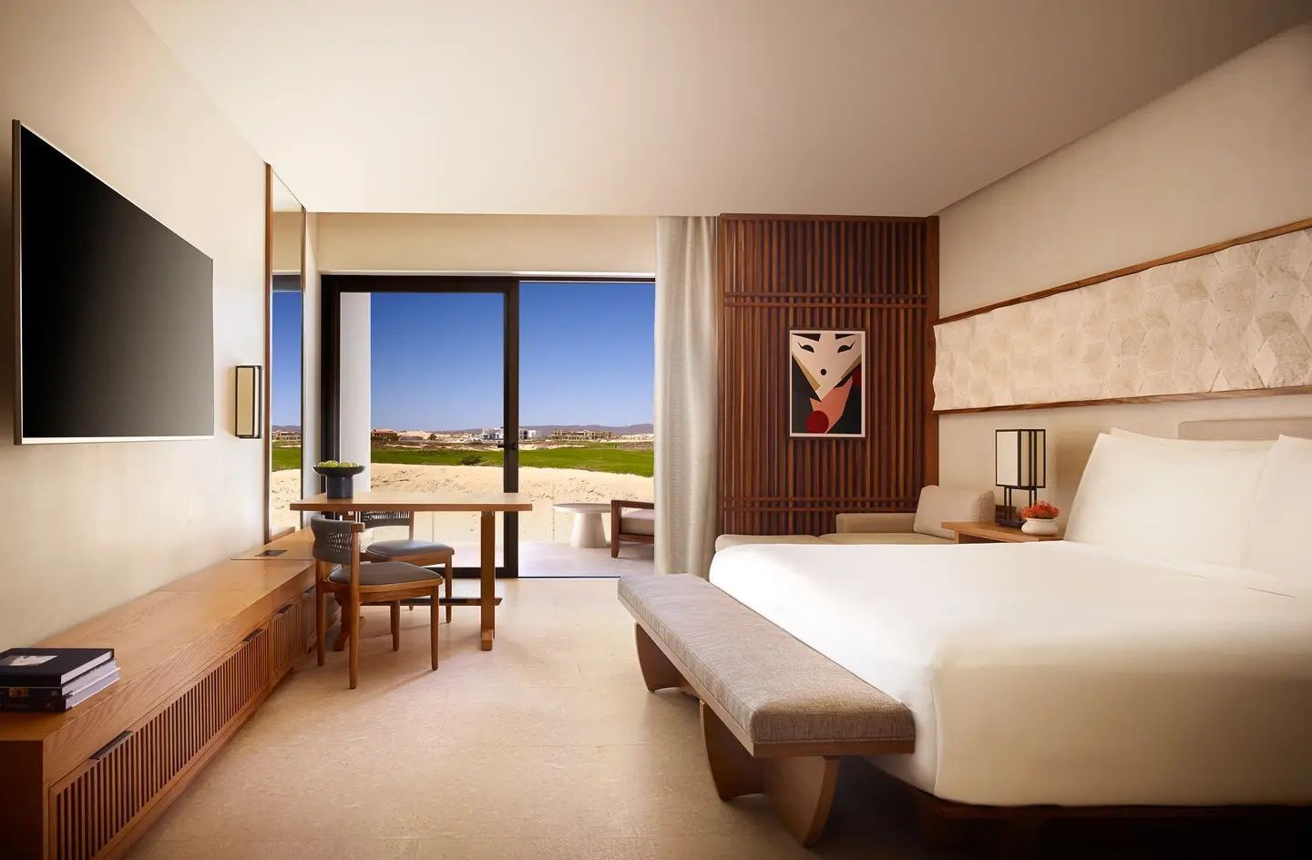 Helles Hotelzimmer mit Doppelbett, Sitzbereich und Balkontür mit Blick auf die Landschaft.