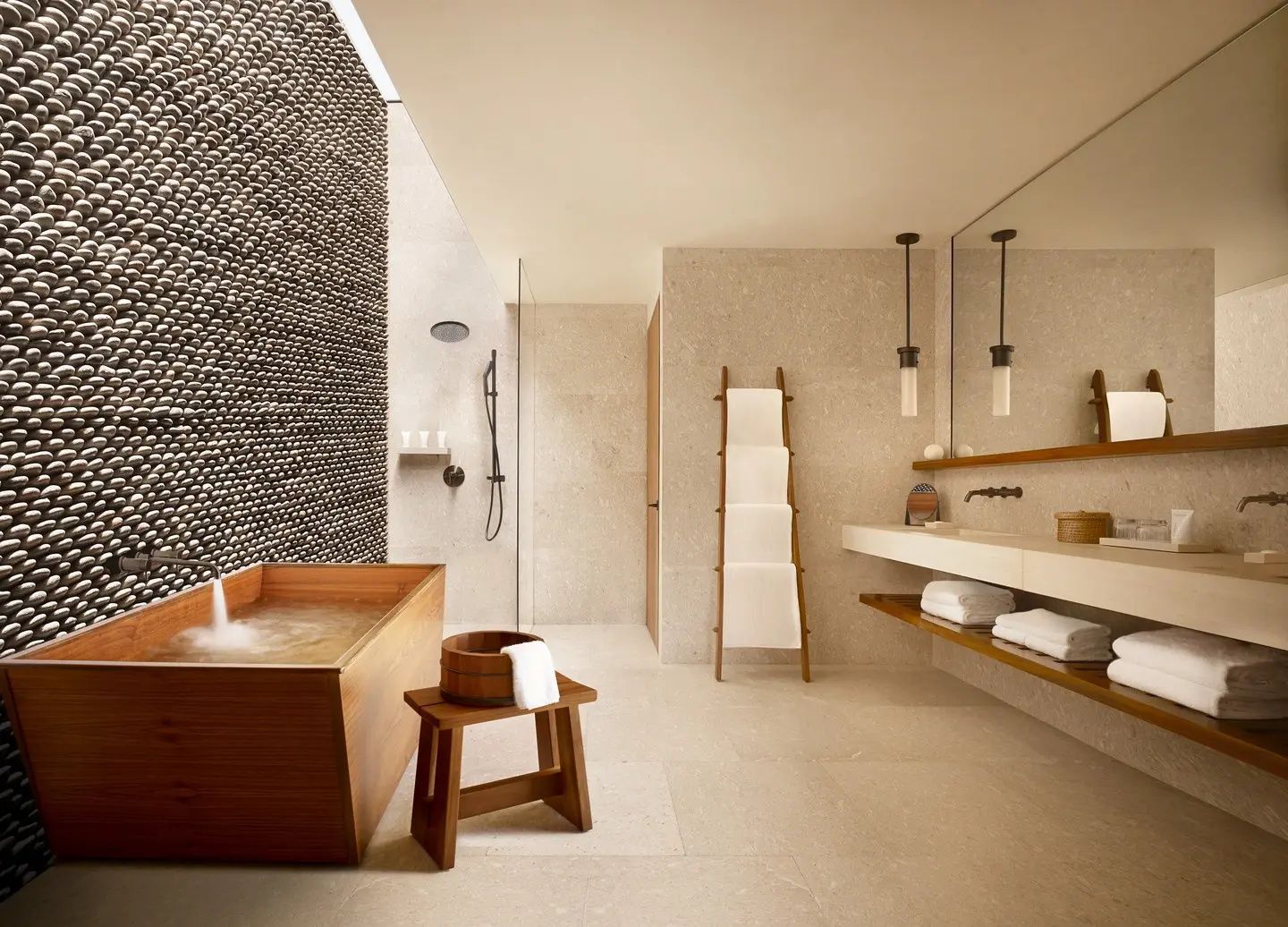 Badezimmer mit hölzerner Badewanne, Natursteinwand, Waschtisch und Handtuchleiter aus Holz.