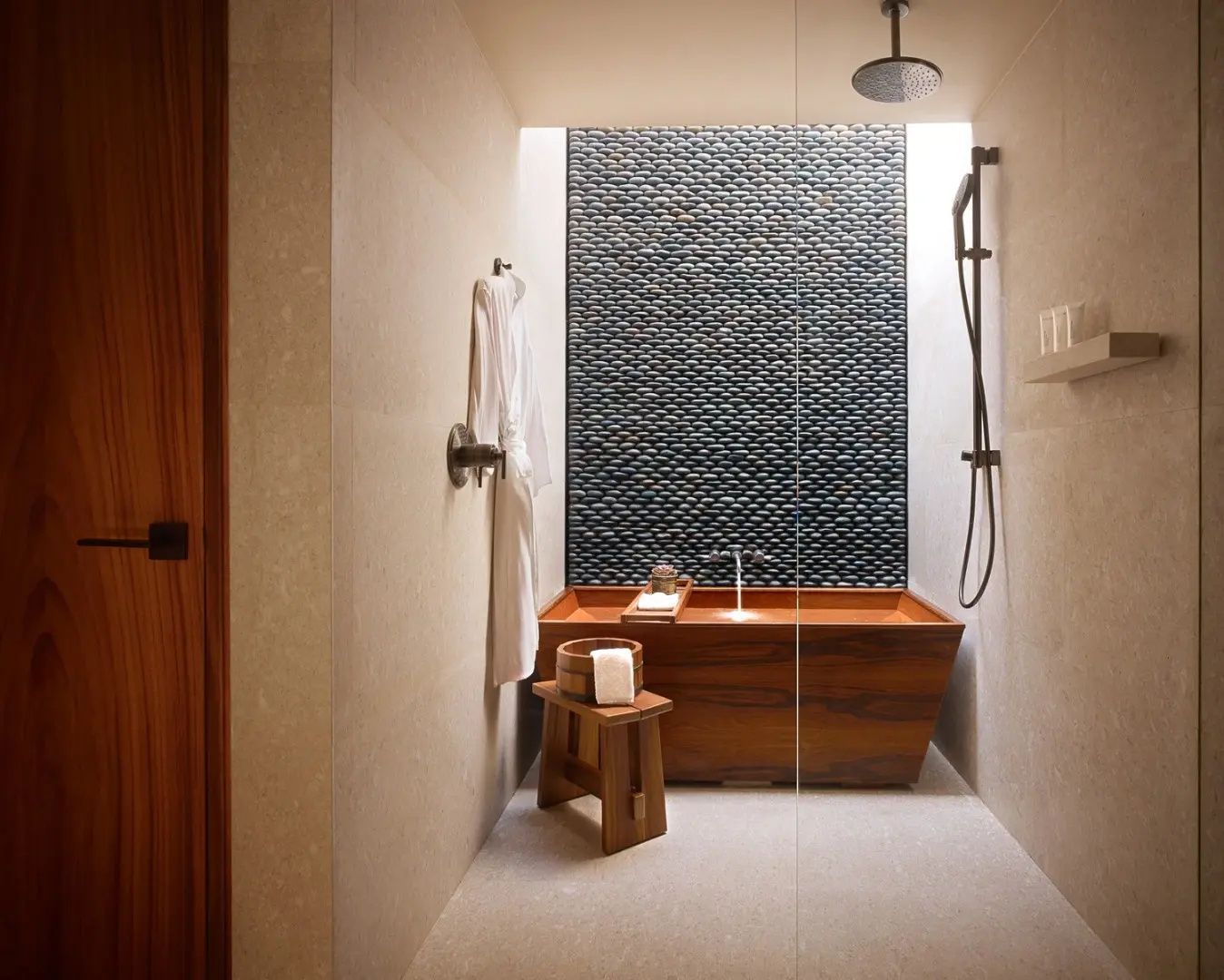 Badezimmer mit einer Holzbadewanne, Regendusche und einer dunklen Natursteinwand.