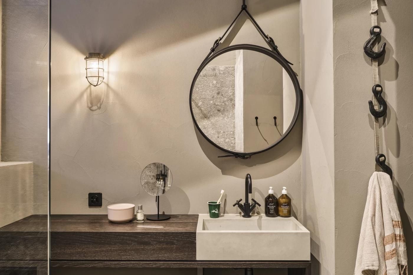 Waschbereich im Badezimmer mit eckigem Waschbecken, dunkler Armatur und rundem Spiegel.