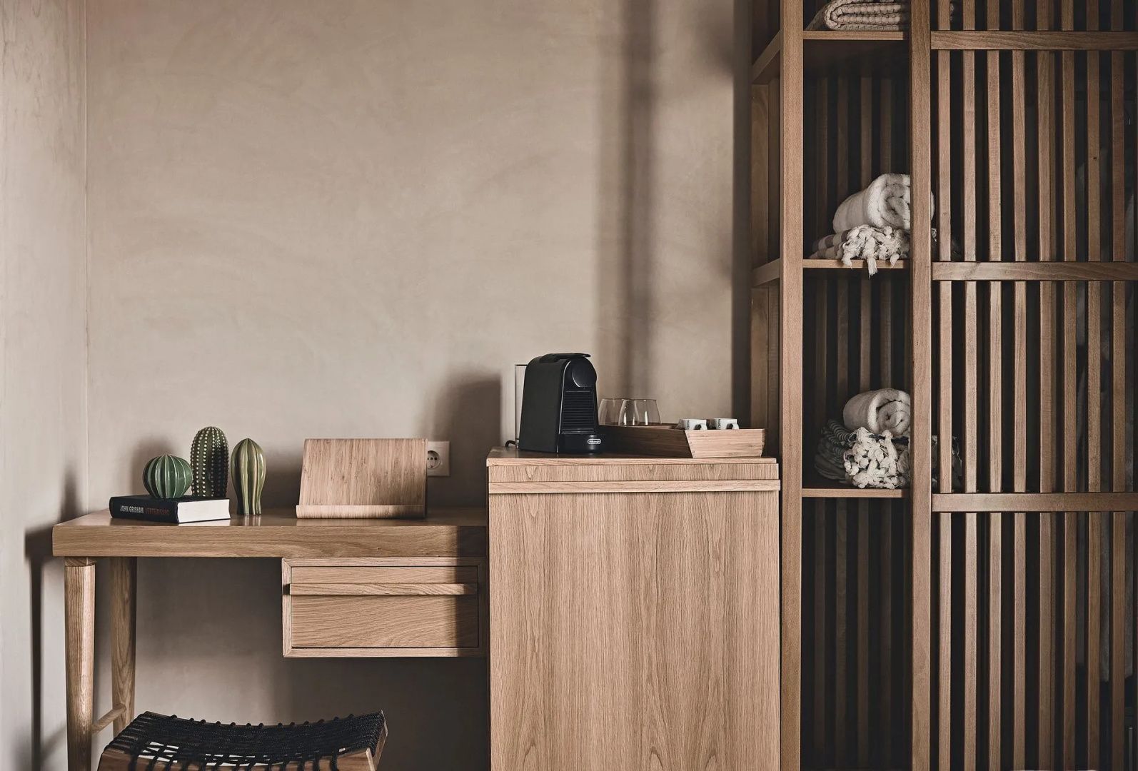 Schreibtisch aus Holz mit Kaffeemaschine, kleinen Kakteen und Regal.