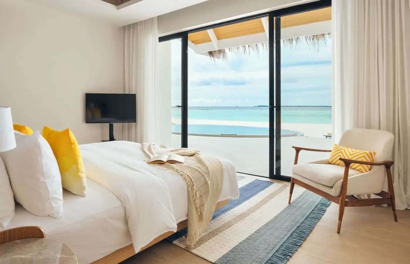 Schlafzimmer mit Doppelbett und Blick über die eigene Terrasse mit Pool auf das Meer und den Strand.