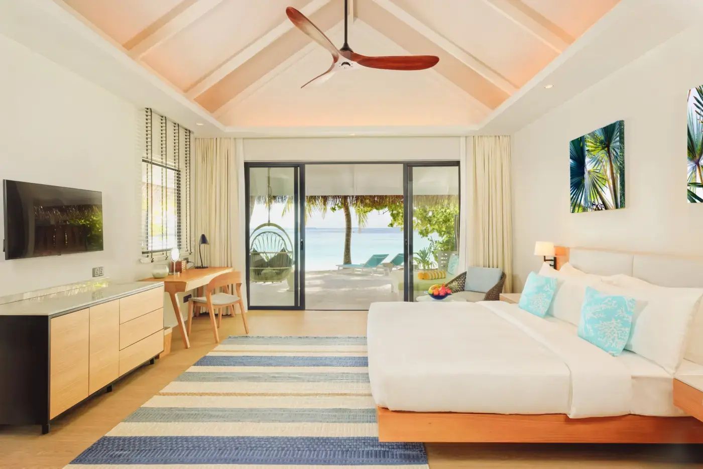 Modernes Hotelzimmer mit großem Bett, Schreibtisch und Blick auf das Meer durch Schiebetüren.