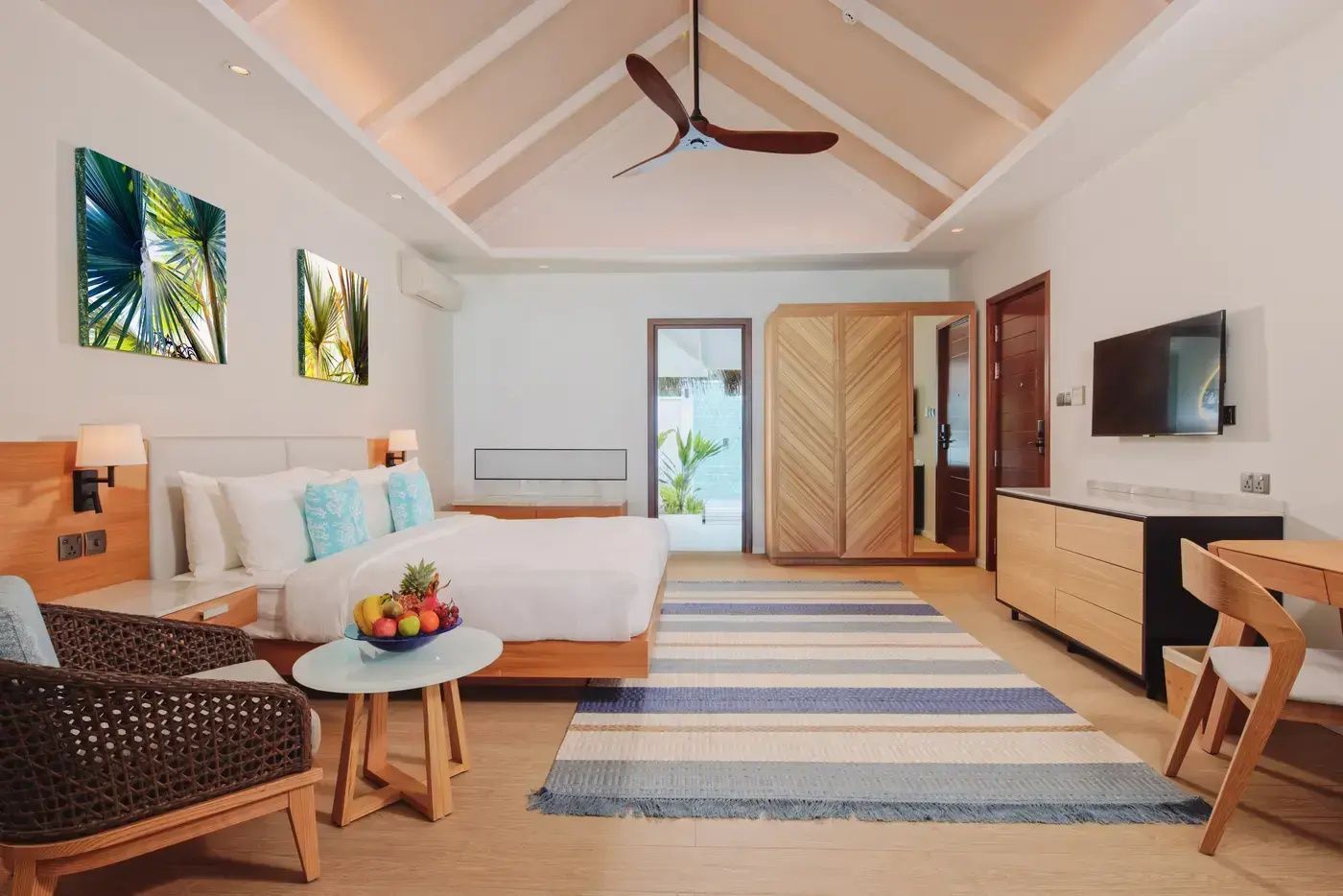 Großzügiges Doppelzimmer mit Holzschrank, Deckenventilator und Tisch mit Obstschale.