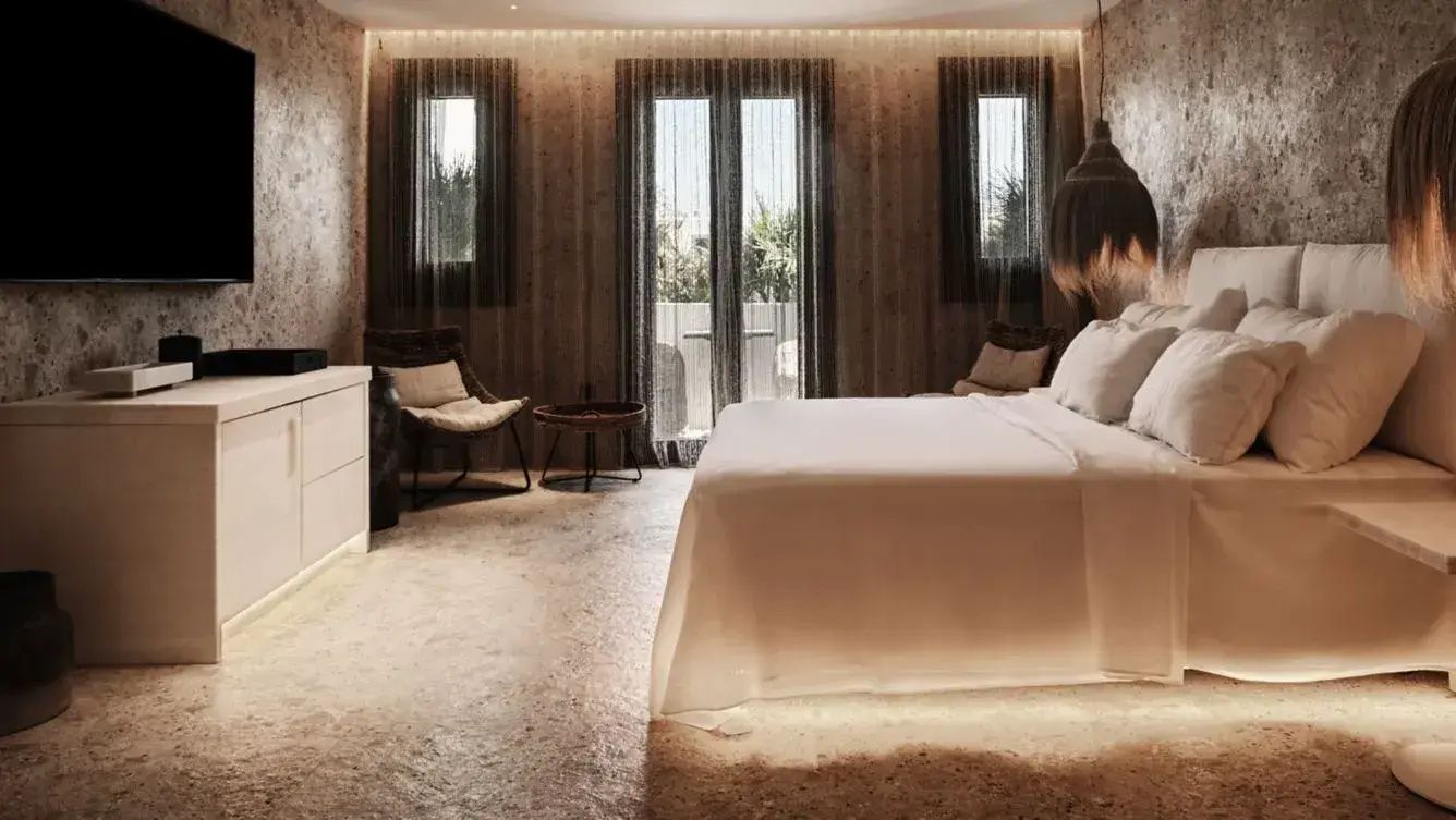 Doppelbett mit weißer Bettwäsche in einem modern eingerichteten Zimmer mit Natursteinoptik.