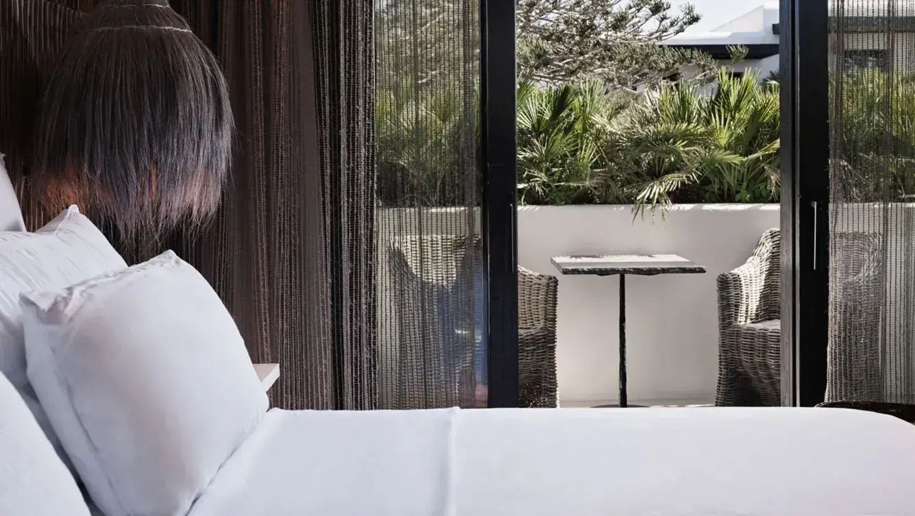 Blick vom Bett durch eine Glastür auf eine kleine Terrasse mit Grünpflanzen.