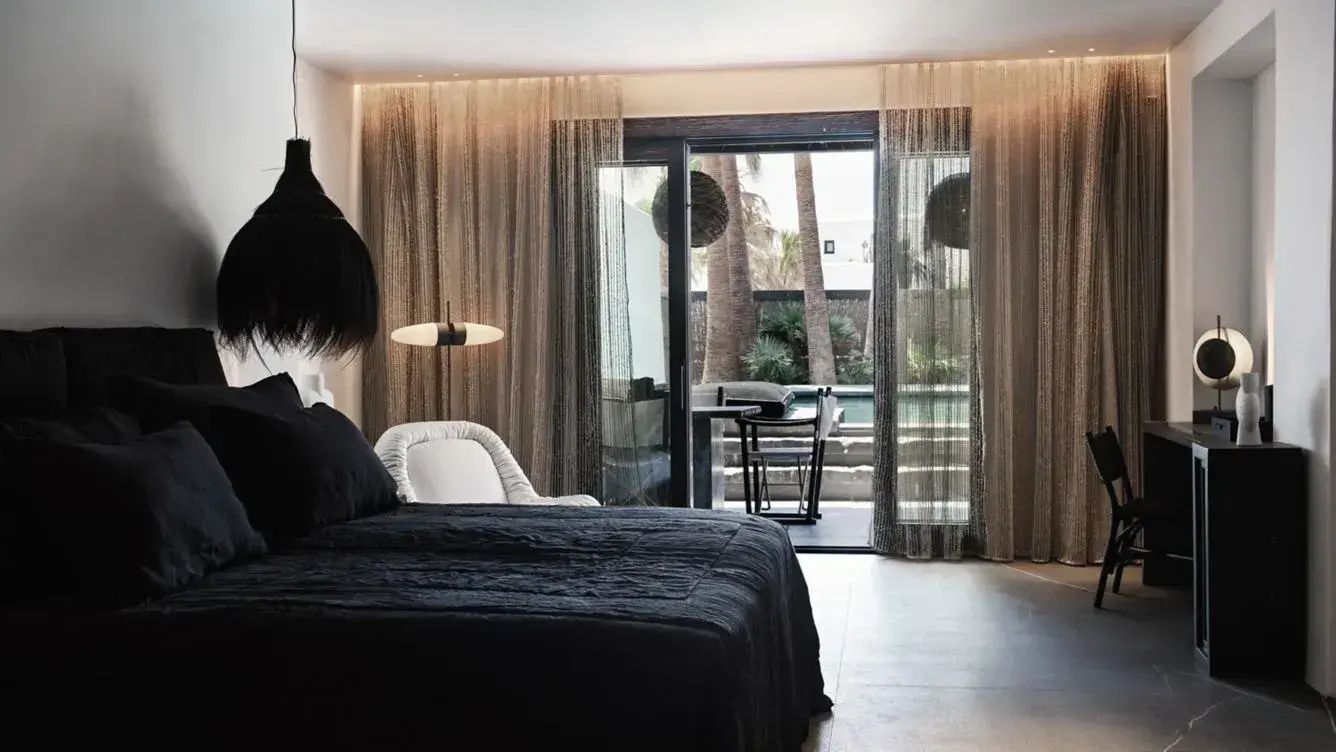 Modernes Schlafzimmer mit schwarzem Bett, weißem Sessel und großer Fensterfront zur Terrasse.