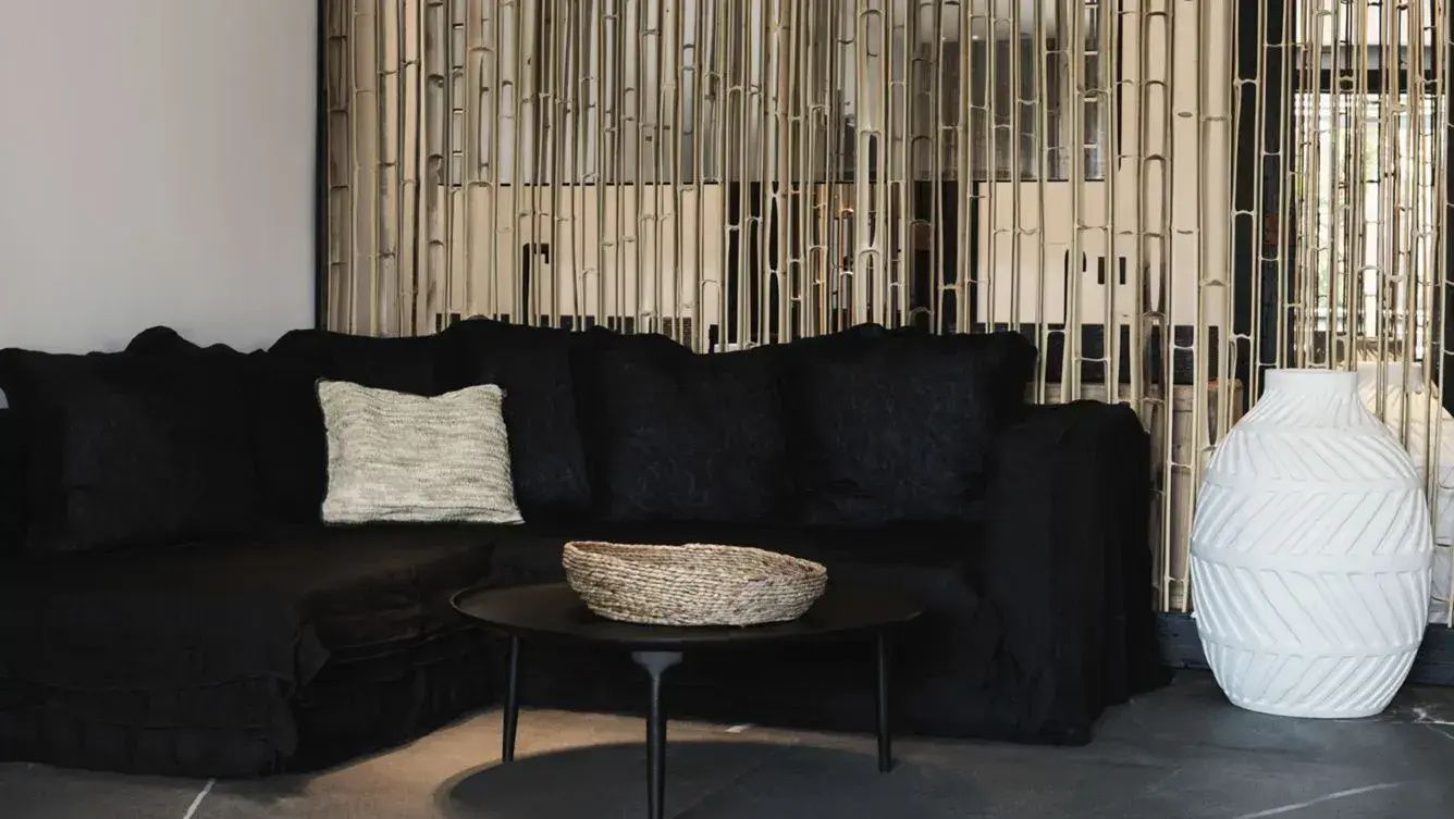 Dunkles Sofa mit hellem Kissen und rundem Tisch vor einer Trennwand aus natürlichen Halmen.