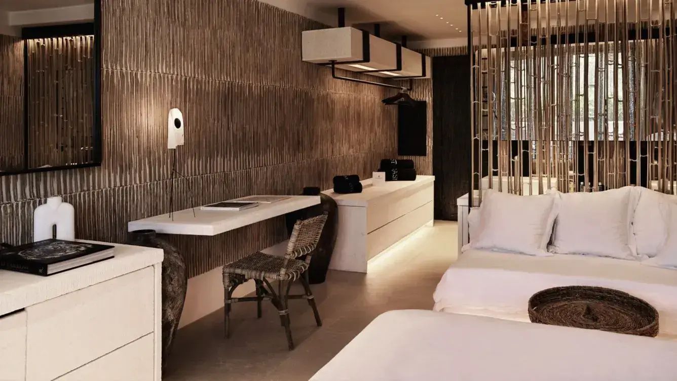 Arbeitsbereich im Hotelzimmer mit weißem Schreibtisch, Flechtsessel und Sideboard.