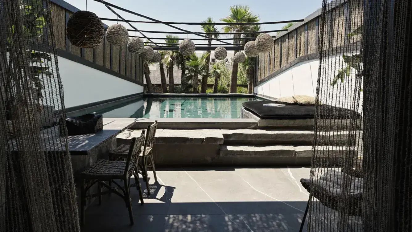 Terrasse mit privatem Pool, Steinstufen, Liegebereich und hängenden Flechtlampen vor Palmen.