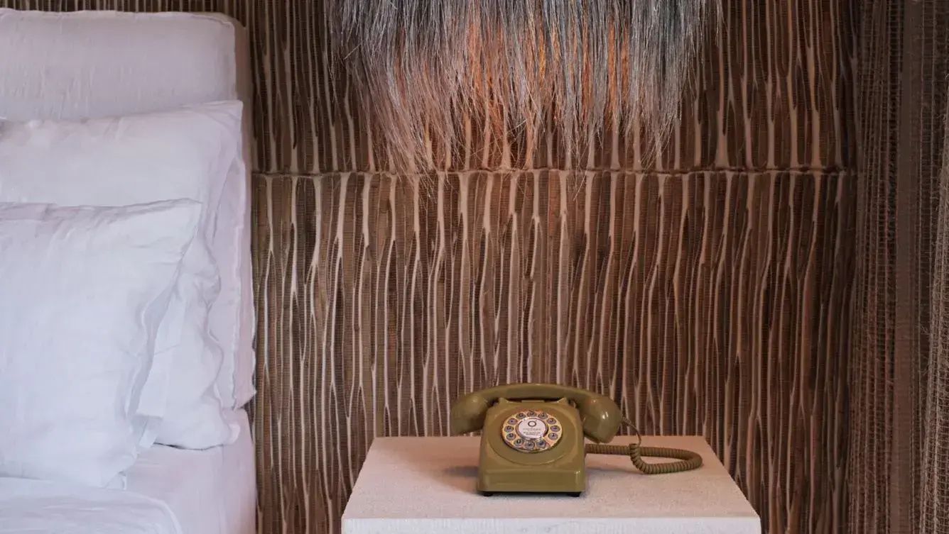 Ein olives Wählscheibentelefon steht auf einem Nachttisch neben dem Bett.