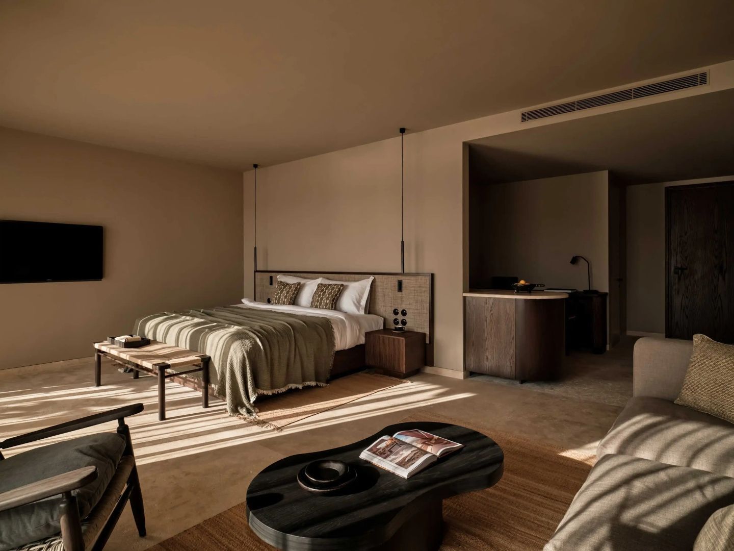 Moderner Hotelraum in warmen Beigetönen mit Doppelbett, Holzmöbeln und Sonnenlicht durch Jalousien.