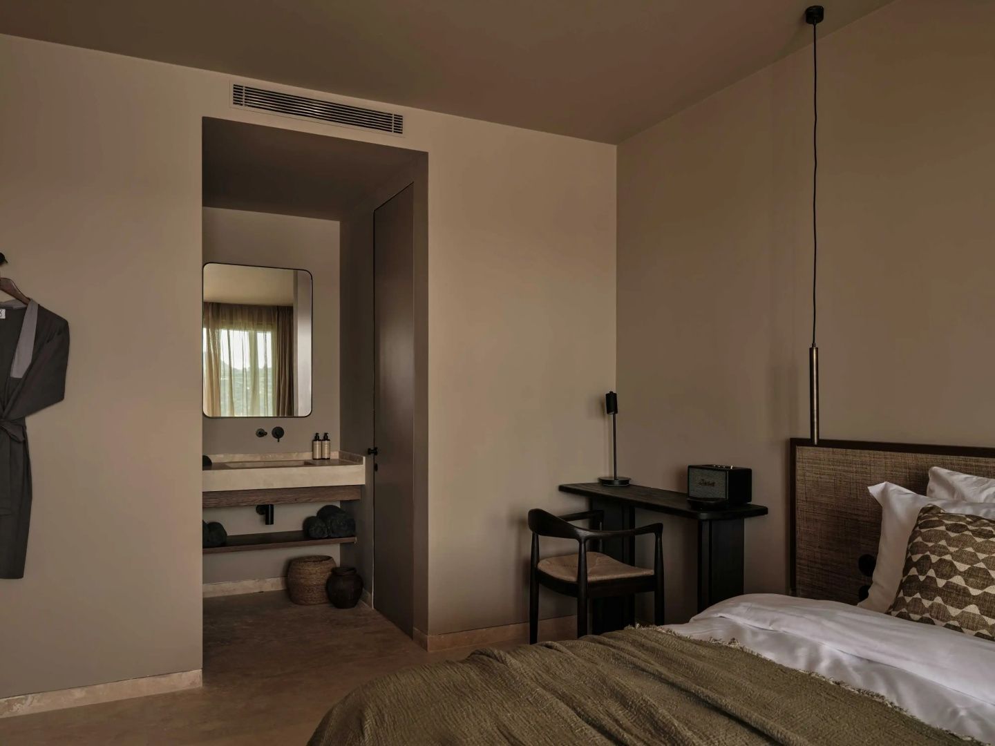 Schreibtisch aus Holz neben dem Bett mit Durchgang zum Badezimmer.