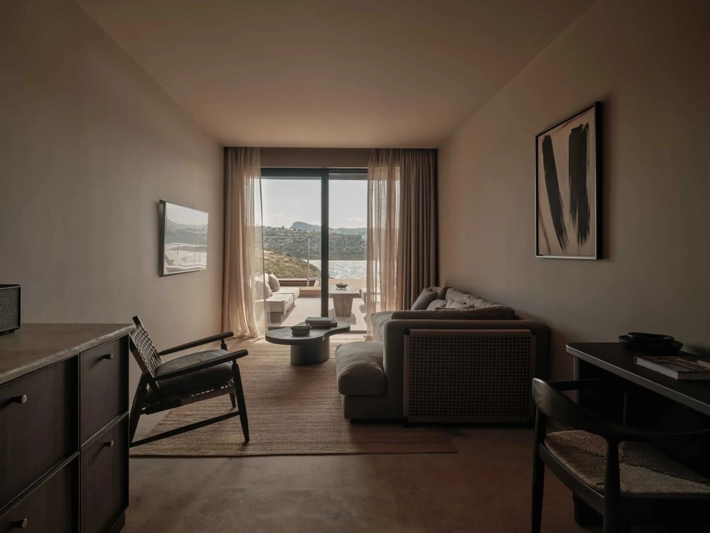 Moderner Wohnbereich mit Sofa, Sessel und Zugang zur Terrasse mit Blick auf das Meer und die Hügel.