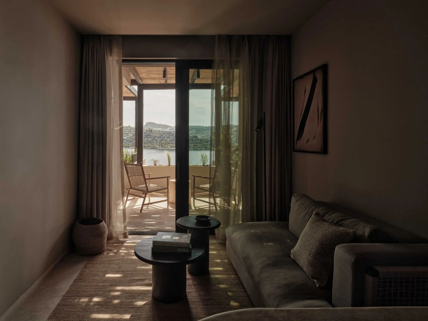 Wohnbereich mit Sofa, zwei beigestellten Couchtischen und Terrasse vor dem Meer.