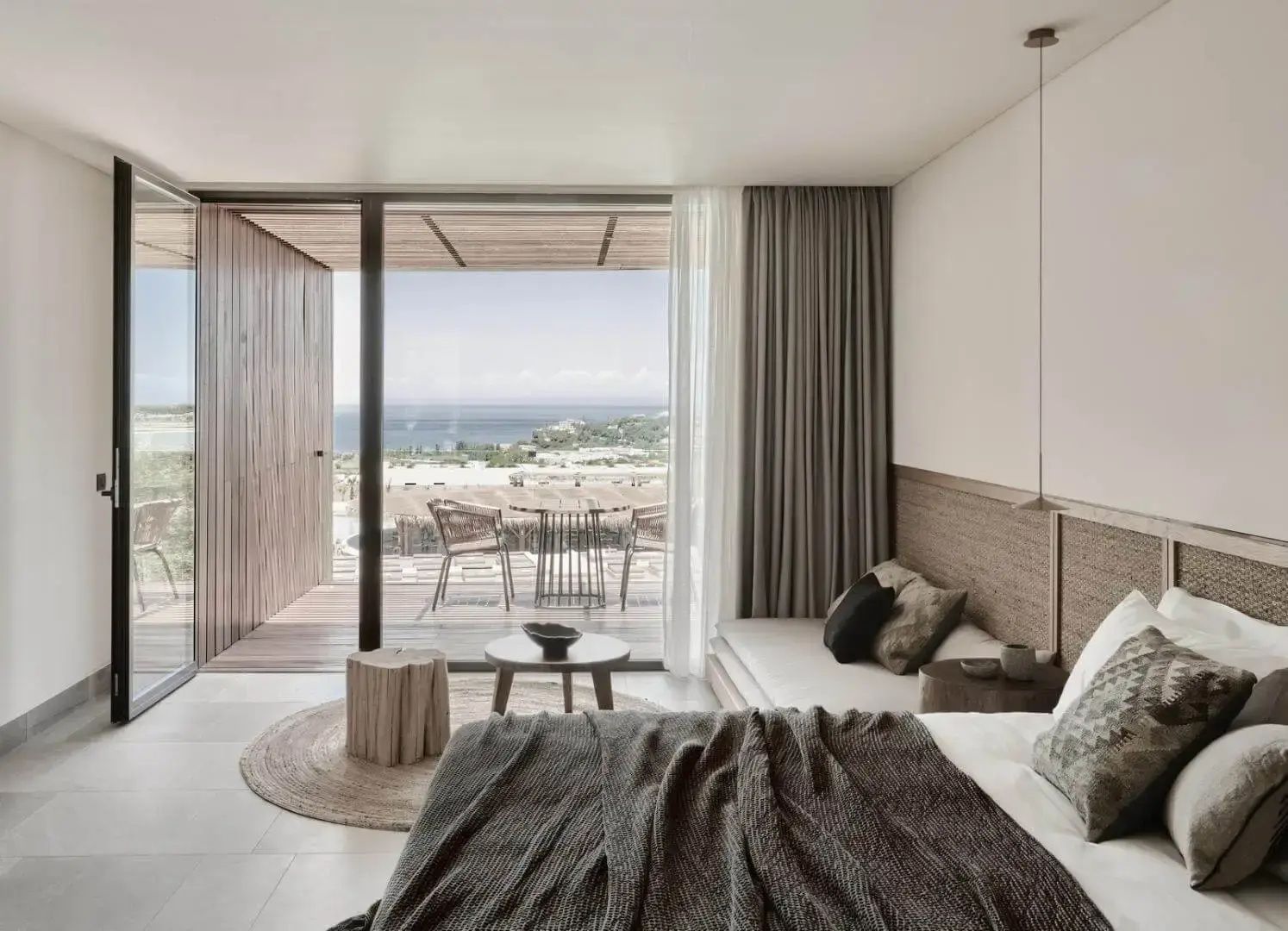 Helles Hotelzimmer mit Doppelbett, Tagesbett und Balkon mit Blick auf das Meer.