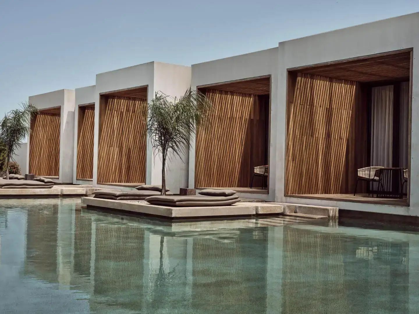 Poolbereich der Hotelanlage mit Liegeflächen und moderner Fassade aus Holz und Beton.