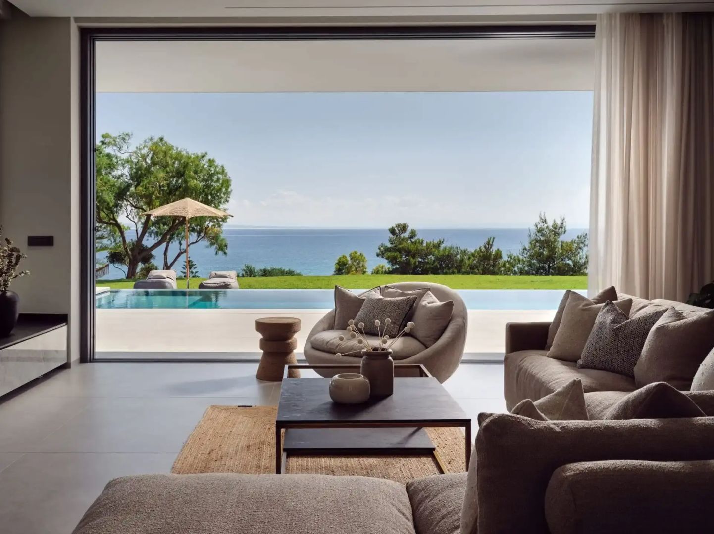 Wohnbereich mit großer Glasfront, Blick auf den Pool und das Meer im Hintergrund.