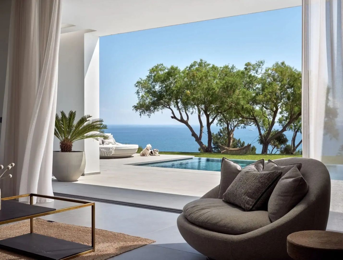 Überdachte Terrasse mit Sesseln und Blick auf den Außenpool sowie das Meer.