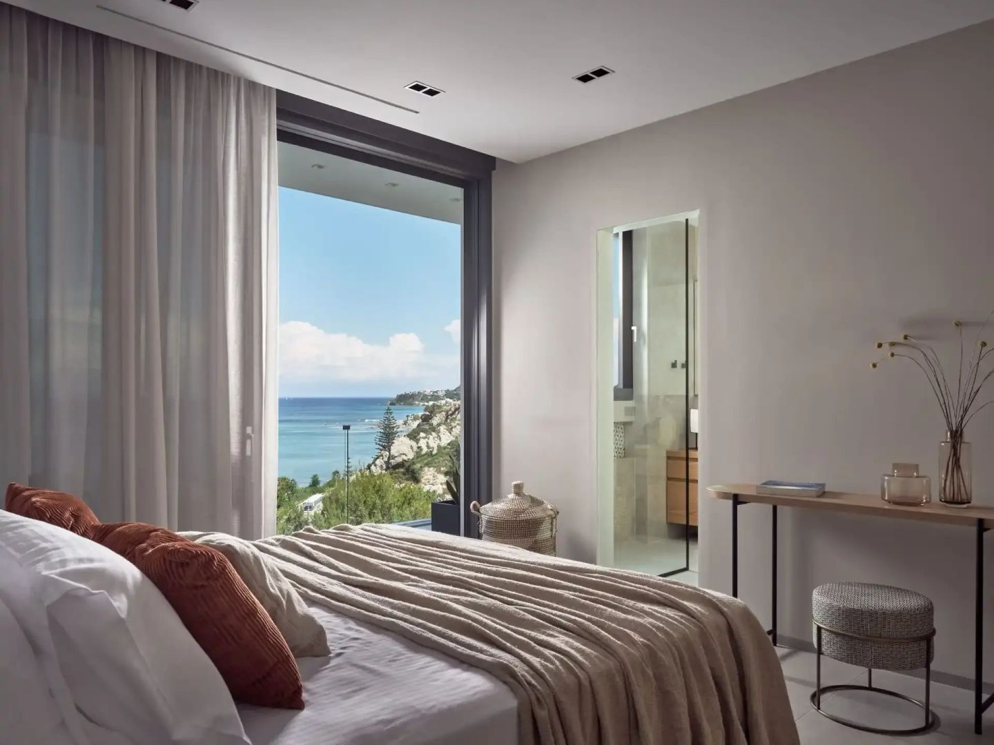 Schlafzimmer mit Doppelbett und bodentiefem Fenster mit Blick auf das Meer.