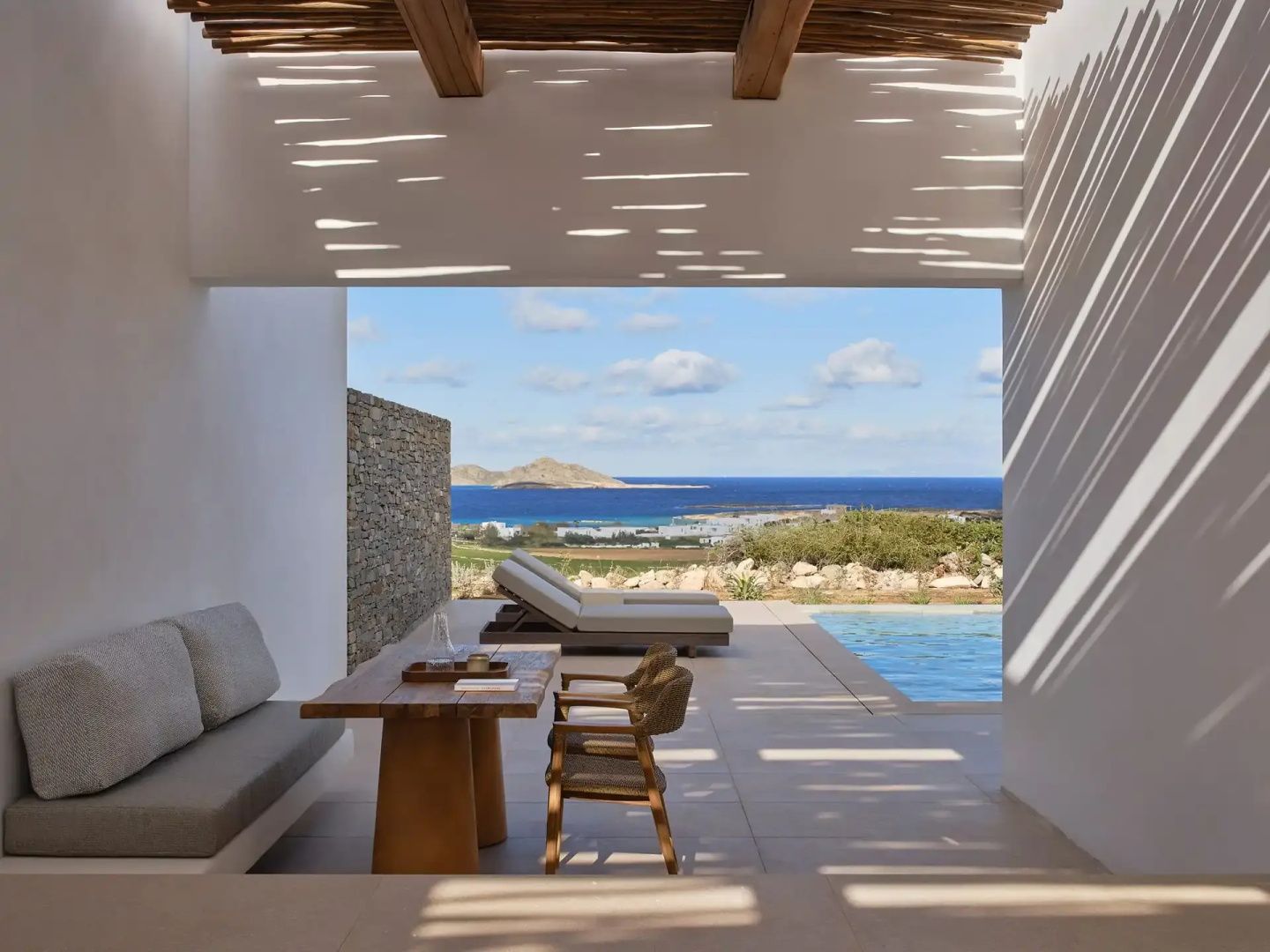 Überdachte Terrasse mit Holztisch und Weitblick über den Pool auf das Meer.