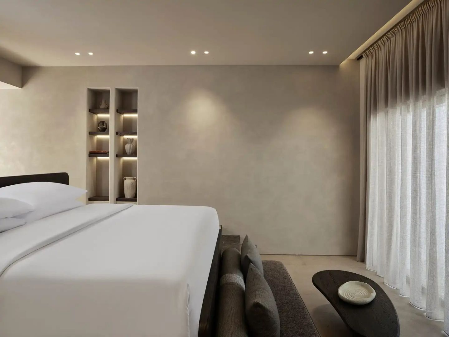 Modernes Hotelzimmer mit Doppelbett, Sitzbank und beigen Wänden mit beleuchteten Nischen.