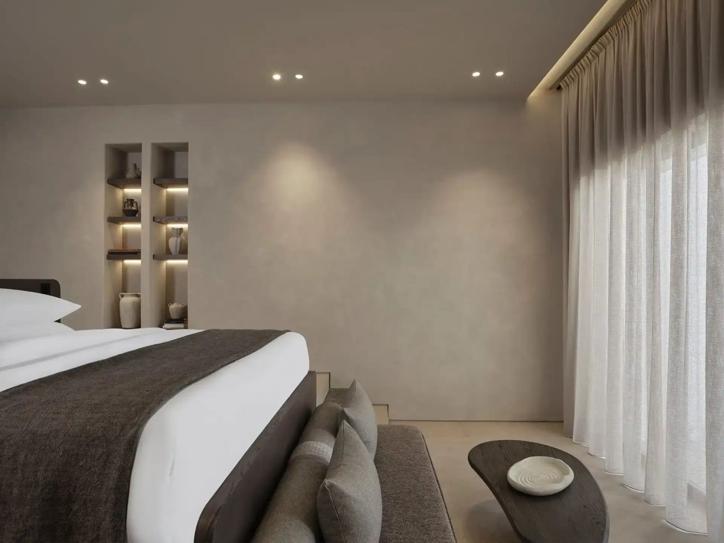 Schlafzimmer mit Doppelbett, dunkler Tagesdecke, beigen Wänden und kleinem Beistelltisch.