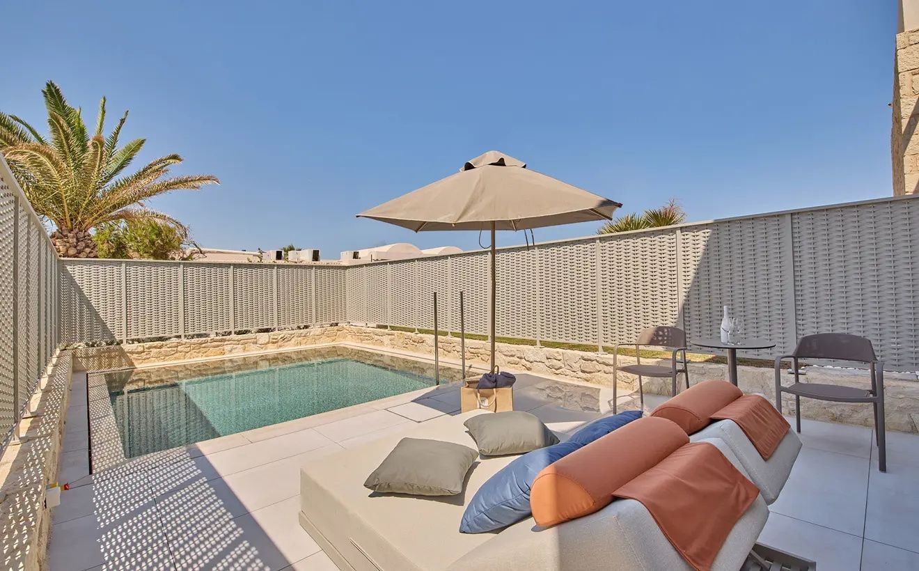 Terrasse mit privatem Pool, Tagesbett mit Kissen und Sonnenschirm unter blauem Himmel.