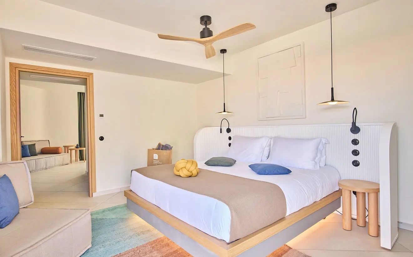 Doppelbett mit weißer Bettwäsche, Holzventilator an der Decke und Hängelampen im Zimmer.