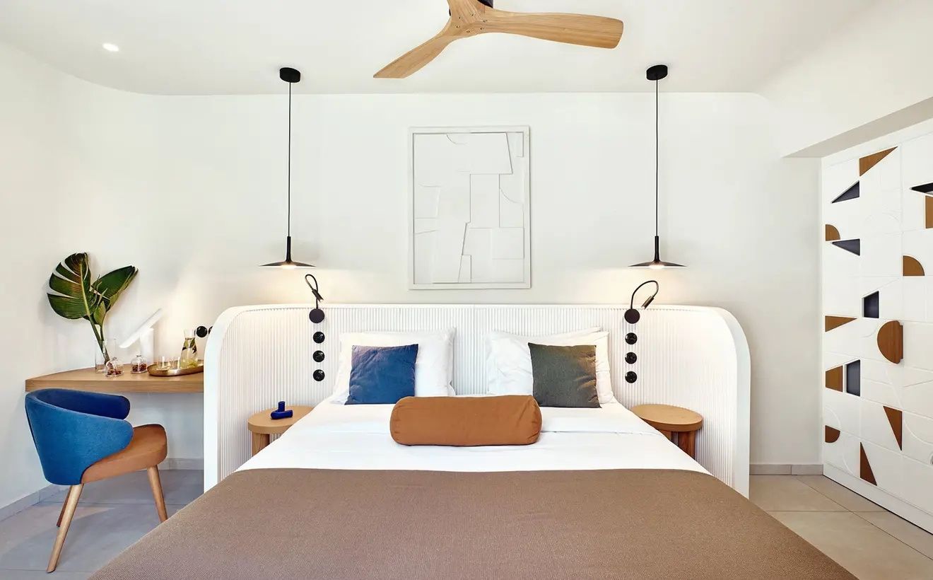Doppelbett mit brauner Tagesdecke, Holzventilator und modernen Nachttischlampen.