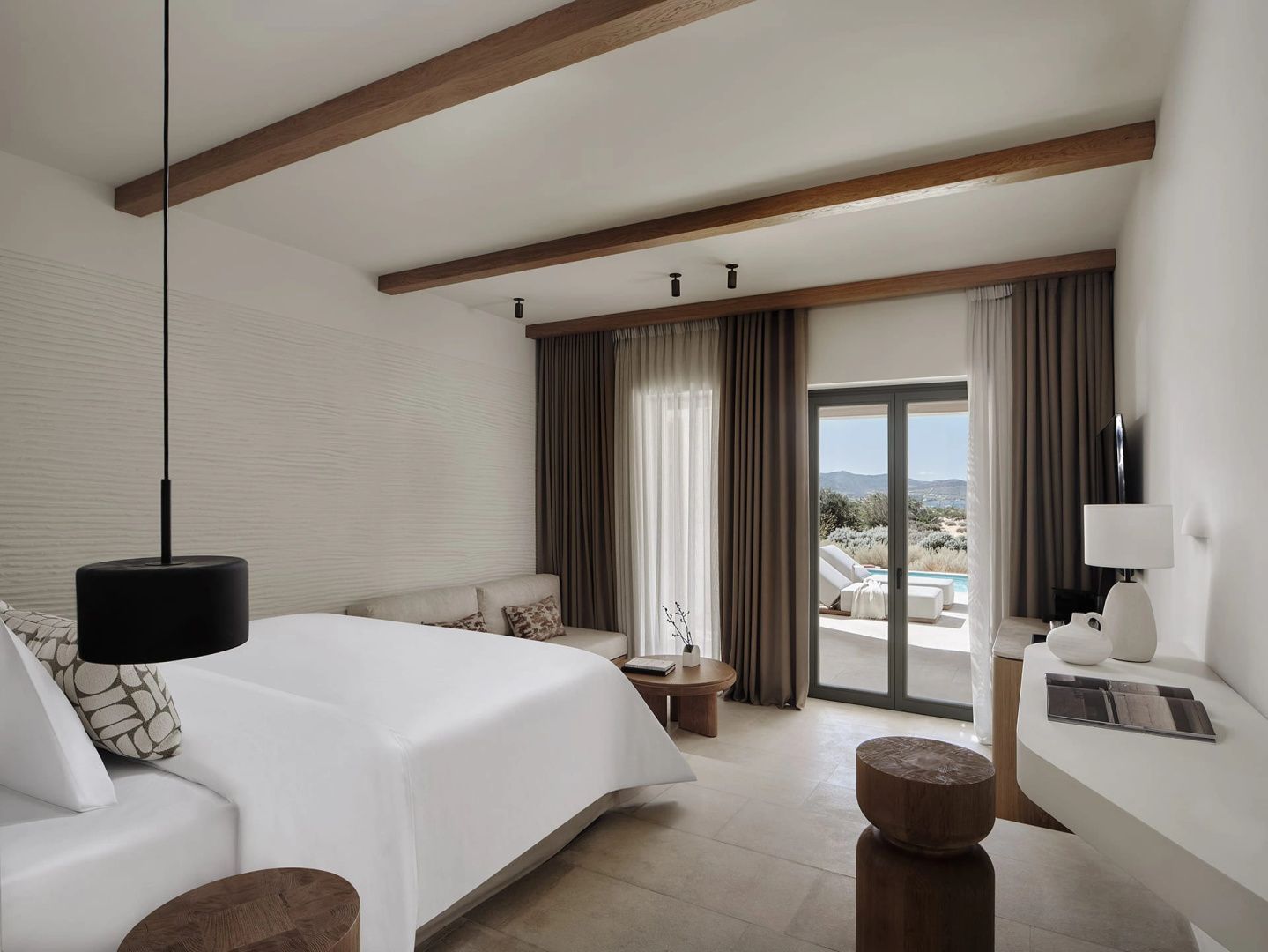Helles Hotelzimmer mit Doppelbett, Holzdeckenbalken und Blick durch die Glasfront auf die Terrasse.