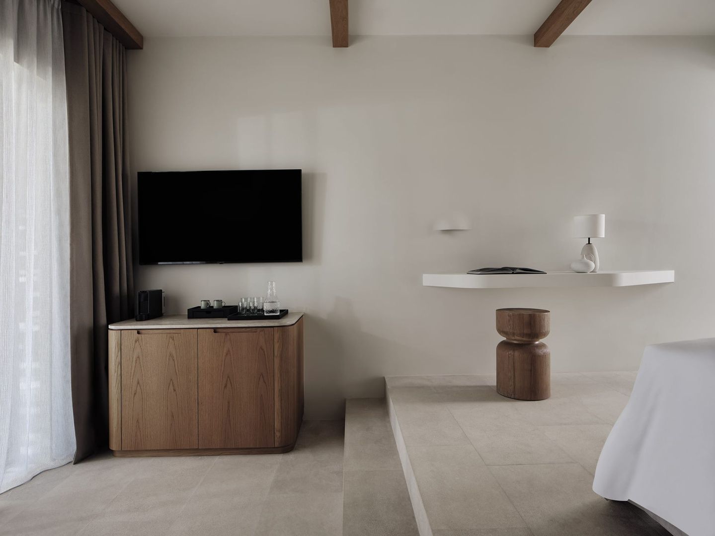 Einrichtung eines Hotelzimmers mit Fernseher, Anrichte aus Holz und einem minimalistischen Sitzbereich.