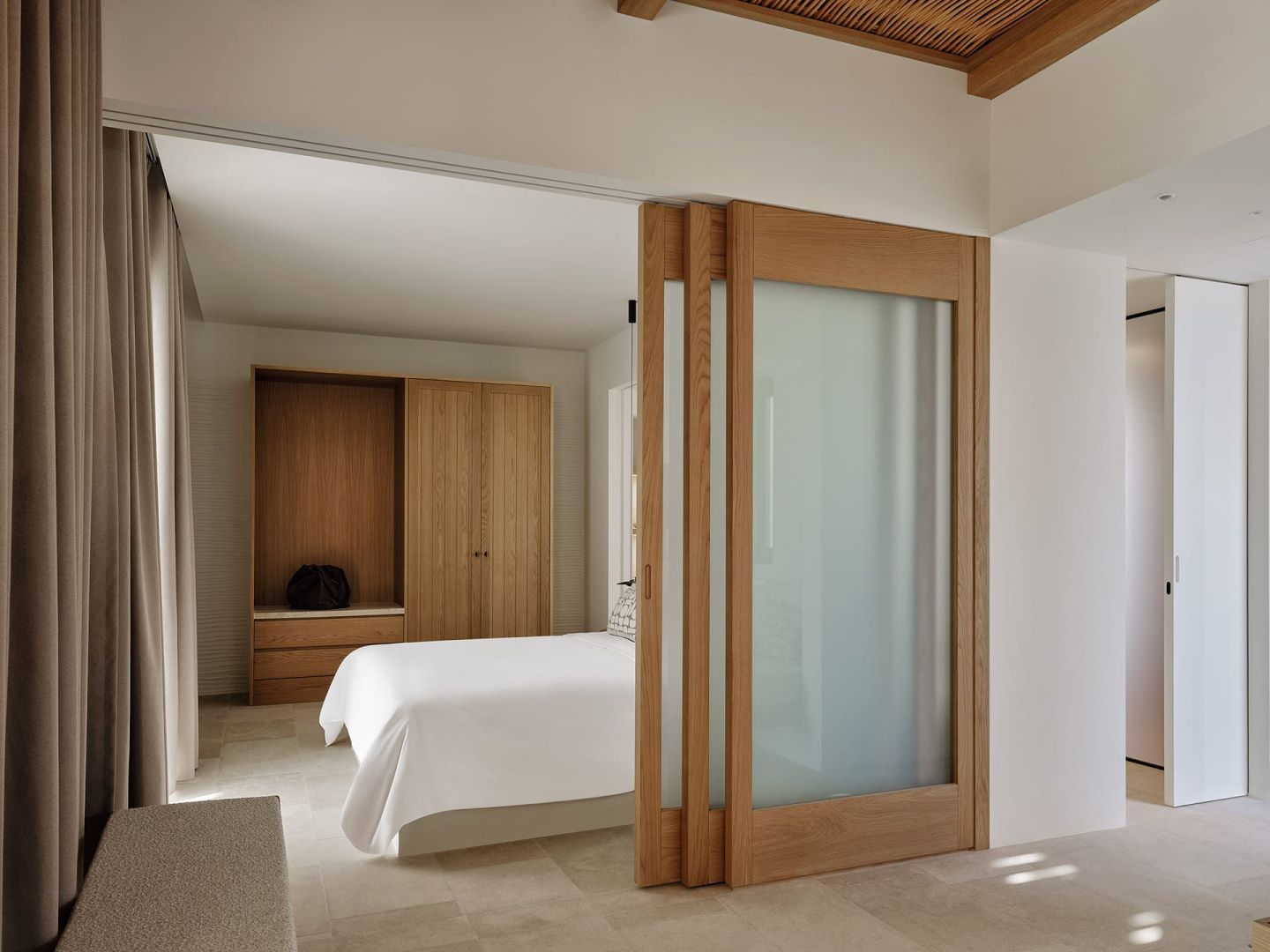 Hell eingerichtetes Schlafzimmer mit Doppelbett, Kleiderschrank aus Holz und Schiebetür.