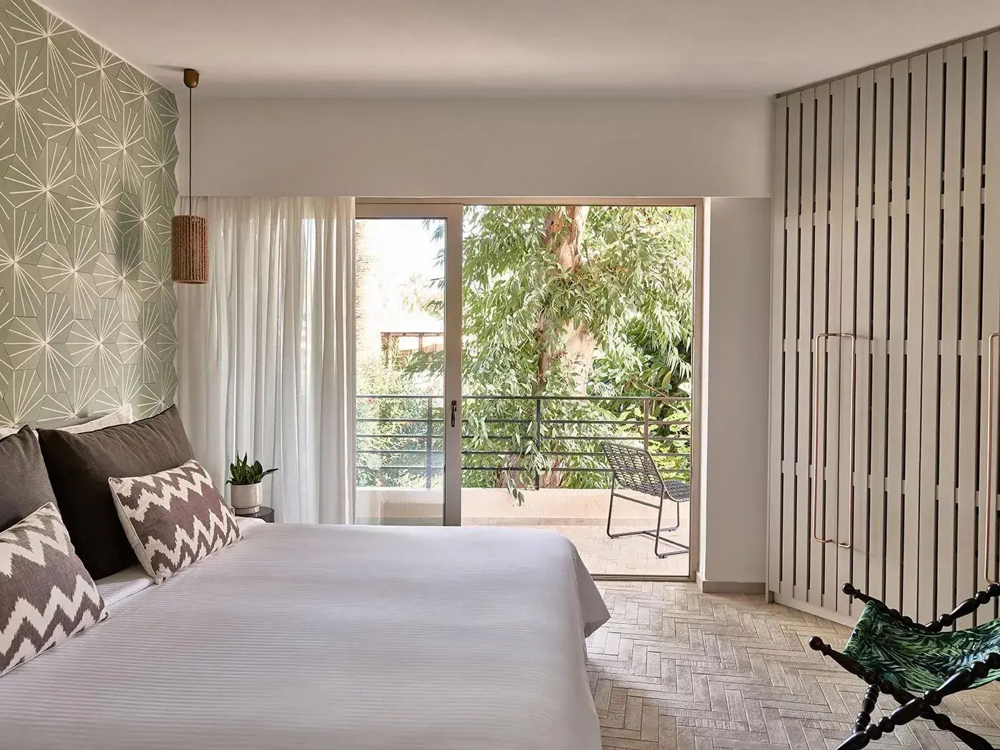 Hell eingerichtetes Schlafzimmer mit Doppelbett und Blick auf den Balkon im Grünen.