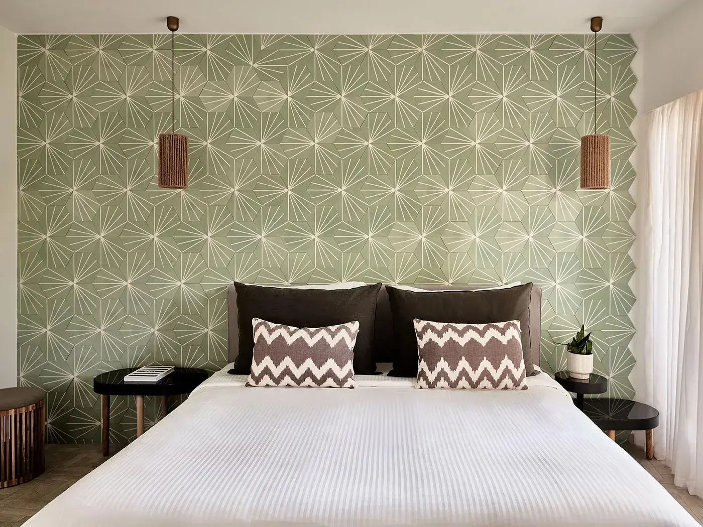 Doppelbett vor einer grünen Wand mit geometrischem Muster und Hängelampen.