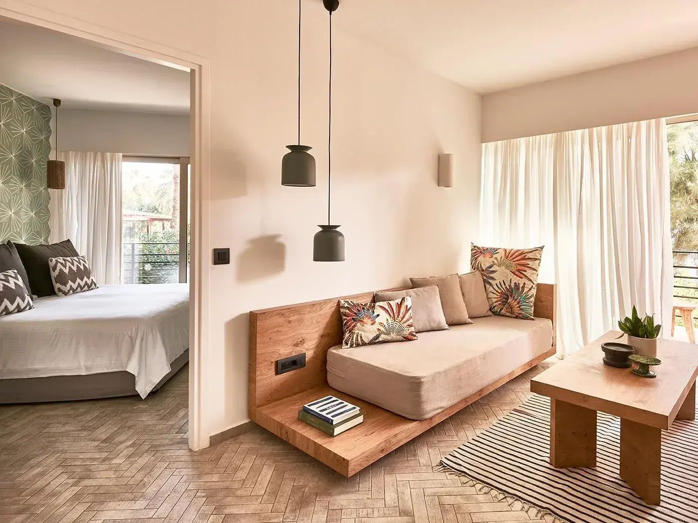 Sitzbereich mit Holzsofa und Kissen sowie Blick in das angrenzende Schlafzimmer.