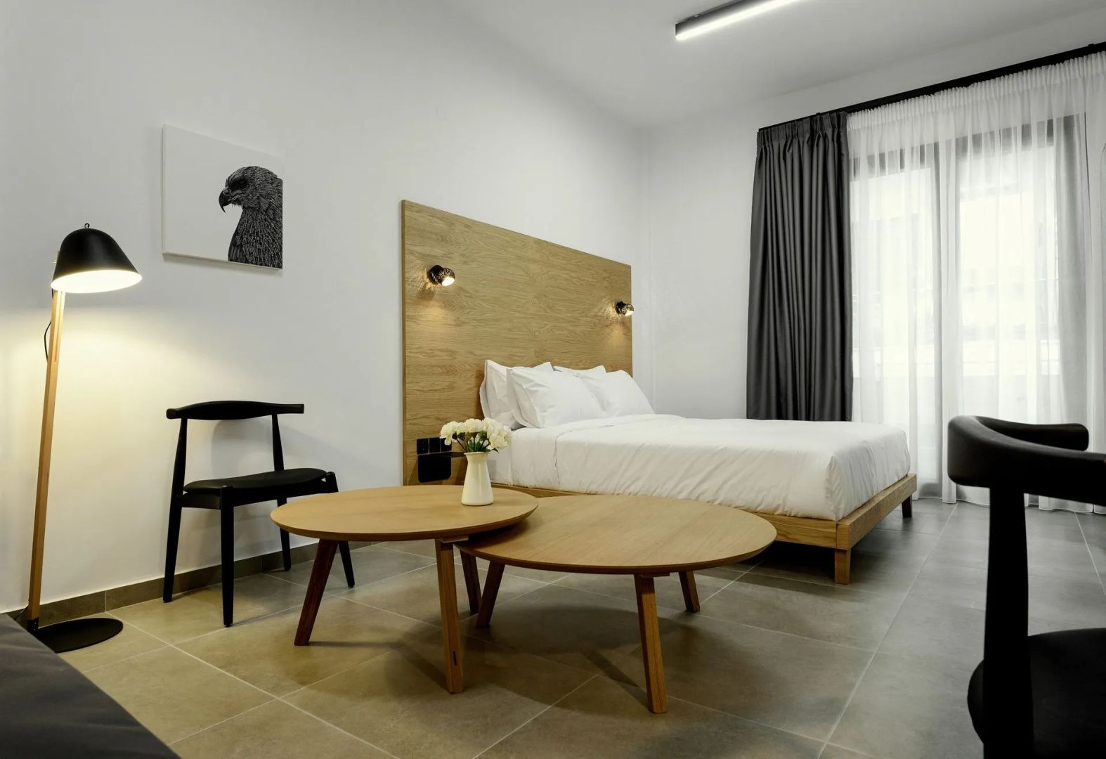 Doppelbett mit Holzkopfteil und zwei runde Holztische mit einer Blumenvase davor.