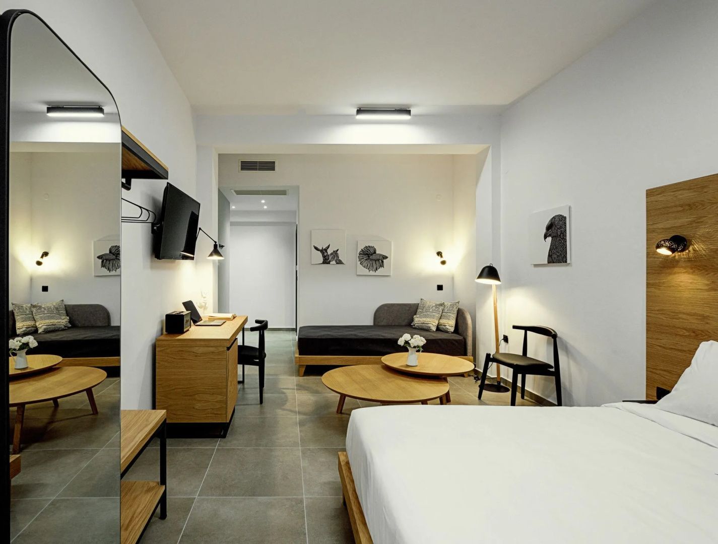 Geräumiges Zimmer mit Bett, Holzmöbeln, Schreibtisch und einer grauen Sitzliege.