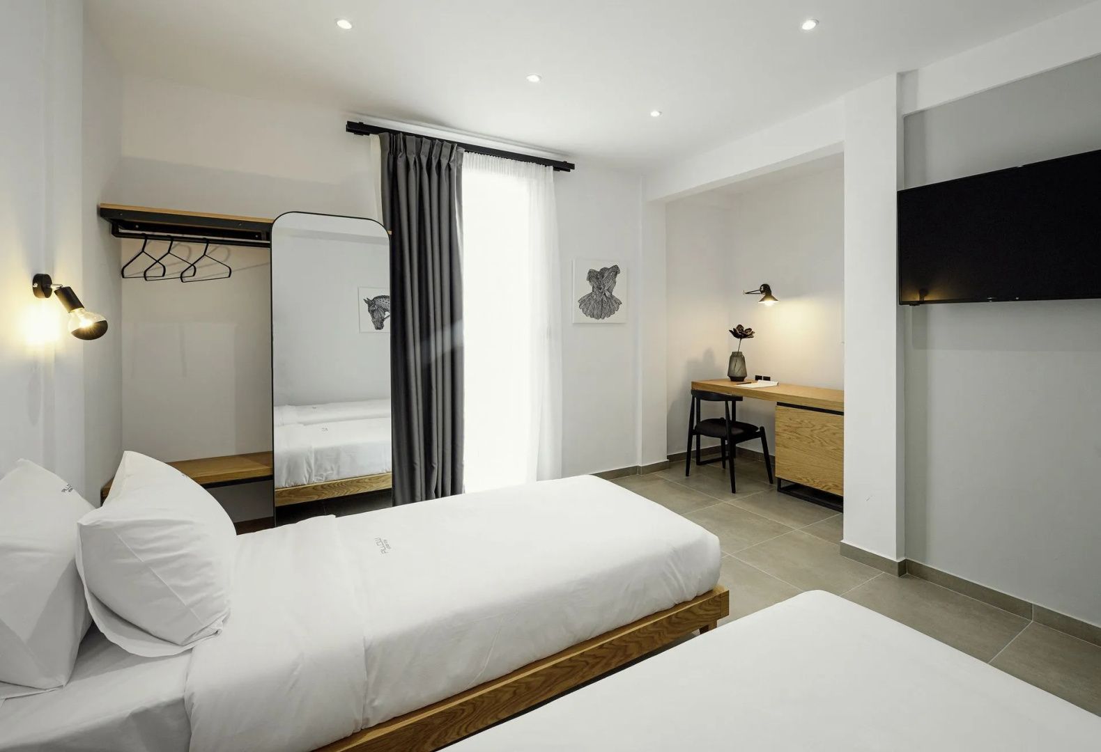 Helles Hotelzimmer mit weiß bezogenen Betten, einem großen Standspiegel und Arbeitsplatz.
