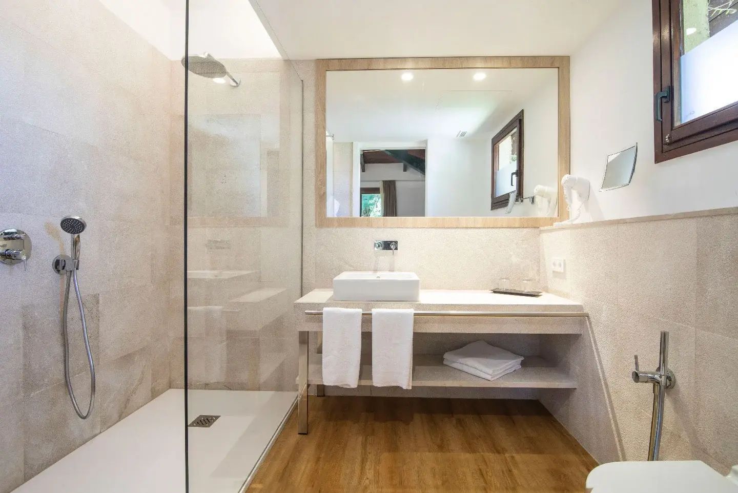 Badezimmer mit bodengleicher Glasdusche, Waschtisch mit rechteckigem Waschbecken und Spiegel.
