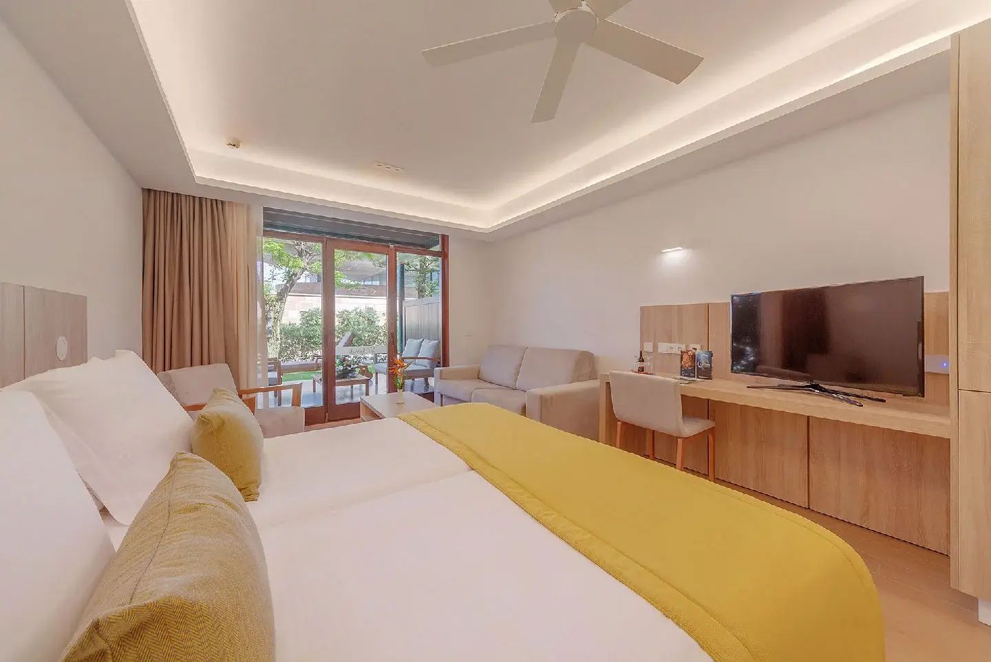 Blick durch das Zimmer auf Bett, Couch, Schreibtisch mit TV und Terrassentür.