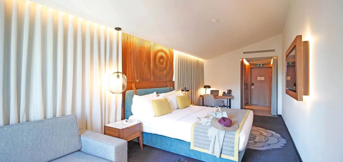 Doppelbett mit gelben Kissen, hölzerner Rückwand und Nachttisch im Hotelzimmer