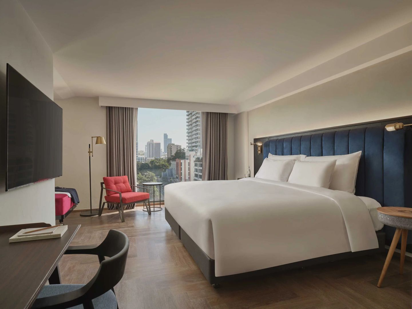 Hotelzimmer mit Doppelbett, rotem Sessel und großem Fenster mit Blick auf die Stadt.