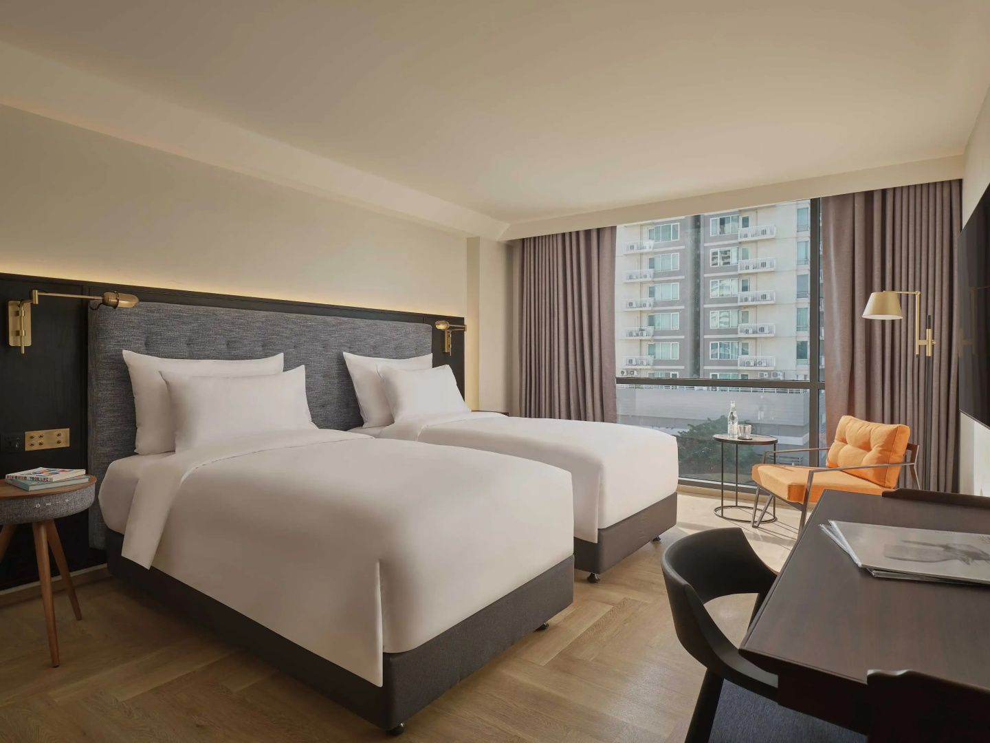 Doppelzimmer mit zwei Einzelbetten, Schreibtisch und Fensterbereich mit Blick auf die Stadt.